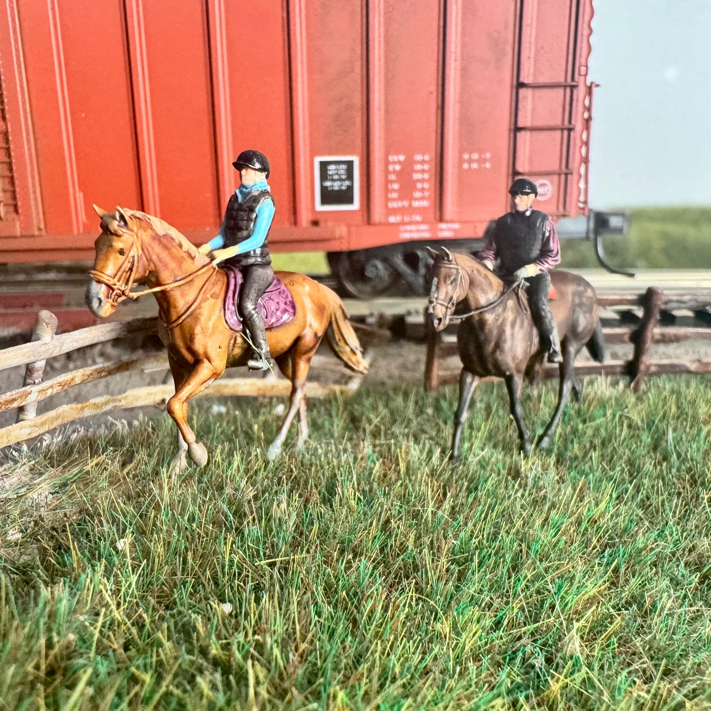 Model horses near a red train car on a grassy area