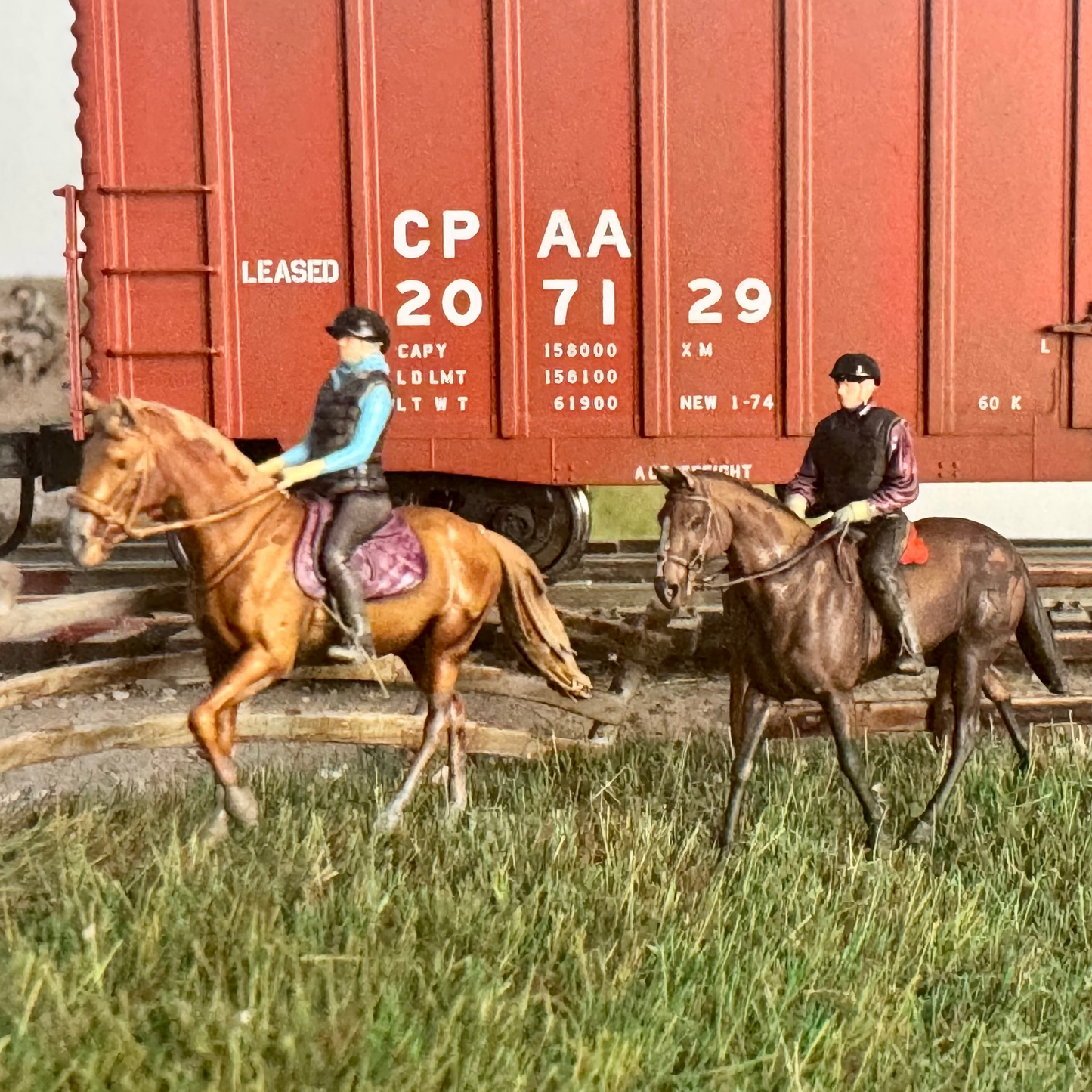 Two people on horseback in front of a red train car with white text.